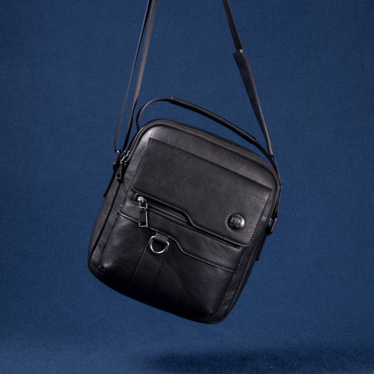 Metro Rover Bag in schwarzem Echtleder mit Fronttasche und Metall-Details vor blauem Hintergrund
