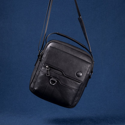 Metro Rover Bag in schwarzem Echtleder mit Fronttasche und Metall-Details vor blauem Hintergrund