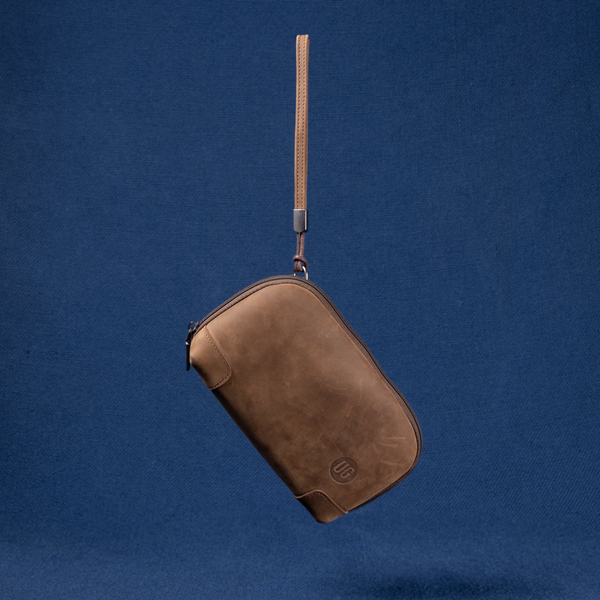 Nomad Pouch in braunem Wildleder – Vorderansicht mit UG Logo